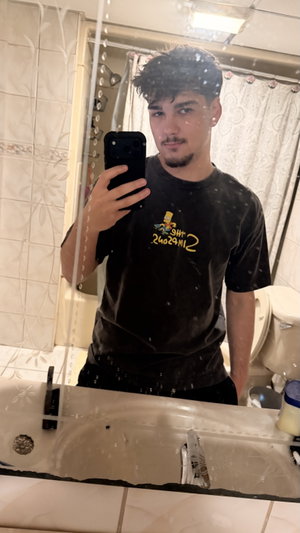 Young man in black t-shirt taking mirror selfie in bathroom.