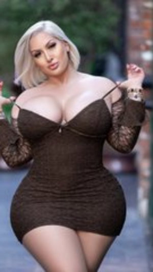 Woman with blonde hair in a brown lace dress posing outdoors.