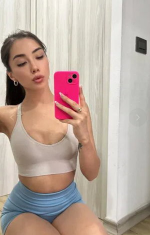 Woman in crop top and shorts taking a selfie indoors.