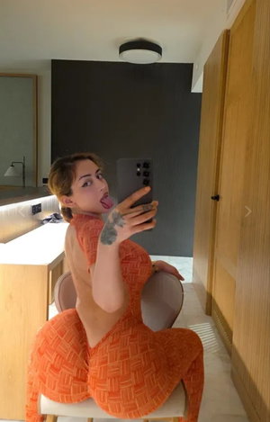 Woman in orange dress taking selfie indoors.