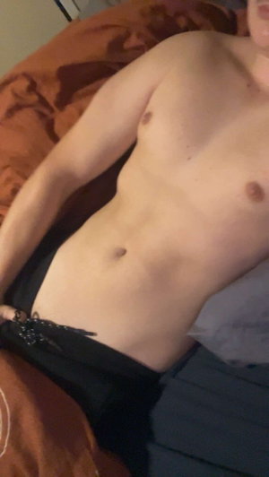 Shirtless man lying on bed, wearing black pants, indoor setting.