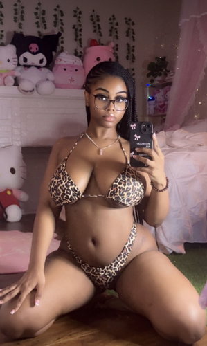 Black woman in leopard bikini taking selfie in bedroom.