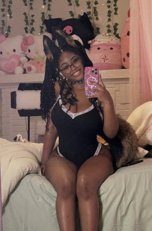 Woman in black bodysuit taking selfie in bedroom with plush toys.