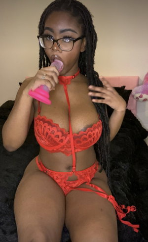 Woman with braids in red lace lingerie holding pink toy, sitting on bed.