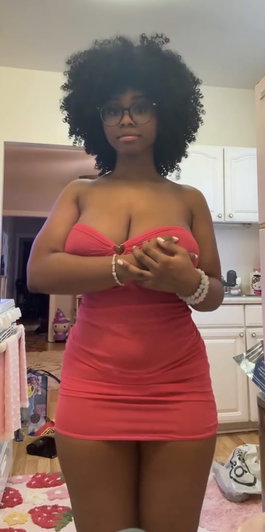 Woman with curly hair in pink strapless dress standing indoors.