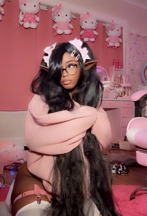 Woman with long black hair and glasses in pink room, wearing pink sweater and white underwear.