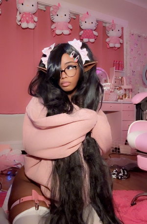 Woman with long black hair and glasses in pink room, wearing pink sweater and white underwear.