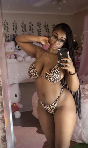 Woman in leopard bikini taking mirror selfie in bedroom with stuffed animals.