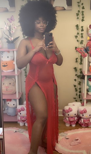 Woman with afro hair and glasses in red dress taking mirror selfie.