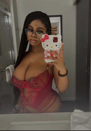 Curvy woman with braids and glasses in red lace lingerie taking mirror selfie.