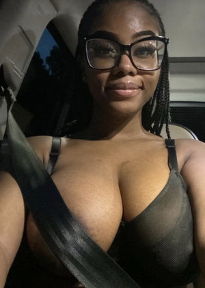 Curvy woman with glasses and braids wearing sheer top in car.
