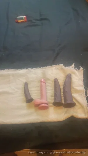 Four sex toys on a white cloth over a dark bedsheet.