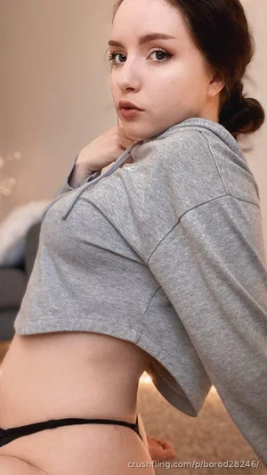 Woman in gray crop hoodie and black underwear posing indoors.
