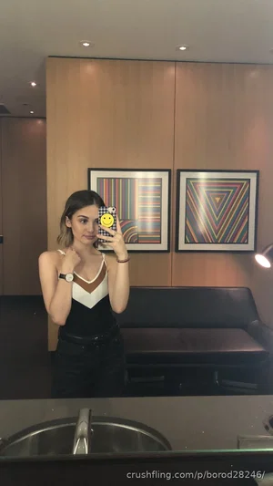 Woman in black and white top, dark pants, taking mirror selfie in modern room with art.
