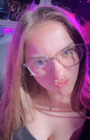 Woman with glasses taking selfie in purple-lit nightclub.