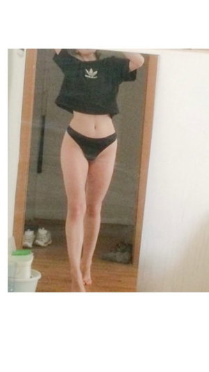 Slim woman in black crop top and panties, mirror selfie indoors.