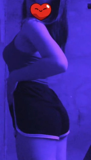Curvy woman in tank top and shorts poses sideways indoors.