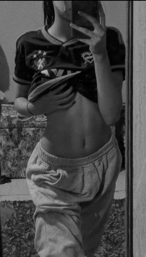 Slim woman in black crop top and gray sweatpants, mirror selfie.