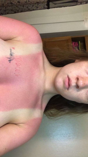 Woman with freckles and shoulder tattoo, topless, lying indoors.
