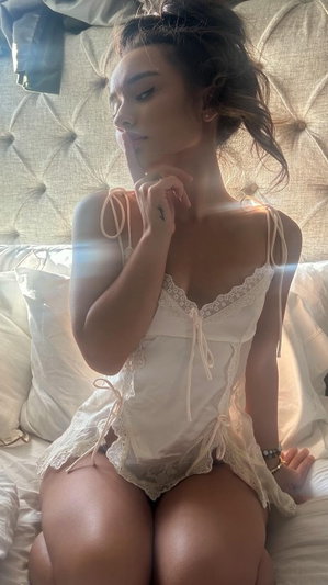 Woman in white lace lingerie sitting on bed with tufted headboard.