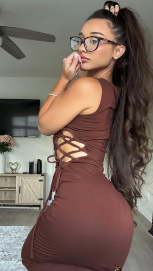 Woman with long dark hair in a brown lace-up dress posing indoors.