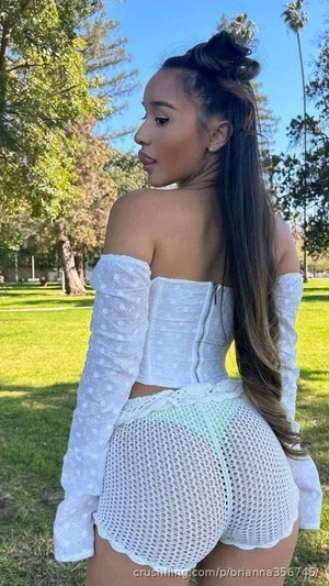 Woman in white off-shoulder top and mesh shorts, standing outdoors in a park.