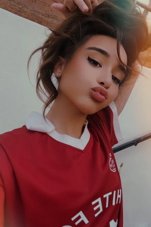 Woman with tousled brown hair in red soccer jersey selfie.