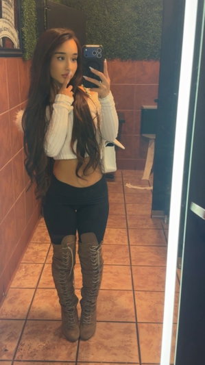 Woman taking mirror selfie wearing white top and black leggings.