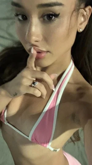 Woman in pink bikini top posing indoors, hand near lips.