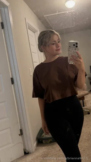 Woman in brown crop top and black pants taking mirror selfie in bedroom.