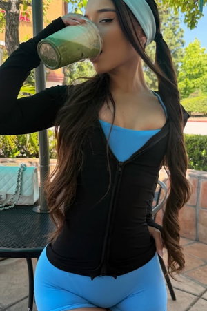 Brunette woman drinking smoothie outdoors in blue activewear.