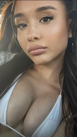 Woman with long dark hair in white top, close-up selfie, indoor setting.