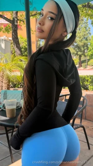 Woman in black hoodie and blue shorts posing outdoors at a cafe.