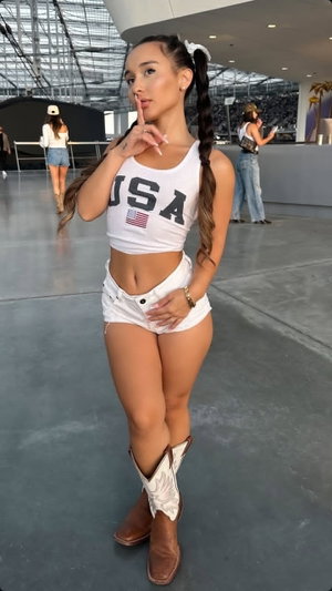 Woman in USA crop top and shorts posing indoors with boots.