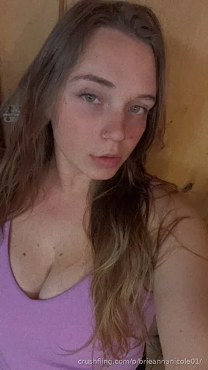 Woman with long brown hair wearing a purple tank top indoors.