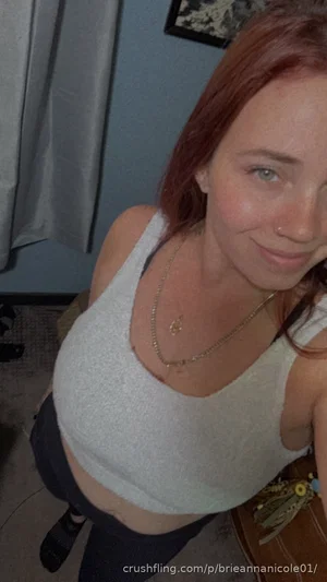 Woman with red hair in a white crop top and dark pants, smiling in an indoor setting.