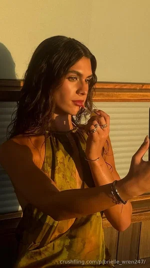 Woman with dark hair in a yellow patterned top, holding phone, indoors.