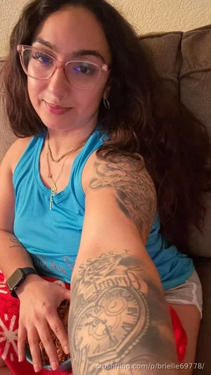 Woman with long dark hair and glasses, wearing blue tank top, sitting on couch with visible arm
