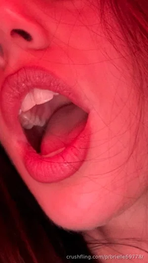 Close-up of a woman's mouth and chin under red lighting, lips parted, teeth visible.