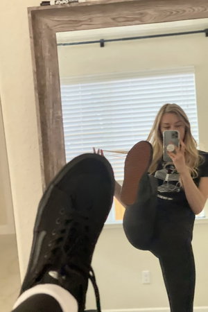 Blonde woman in black t-shirt and leggings in mirror selfie.