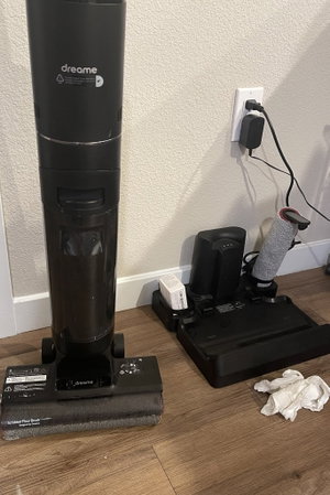 Black Dreame vacuum on wooden floor near charger.