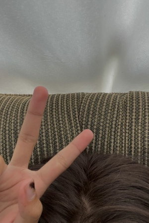 Hands making peace sign near couch, dark hair visible.