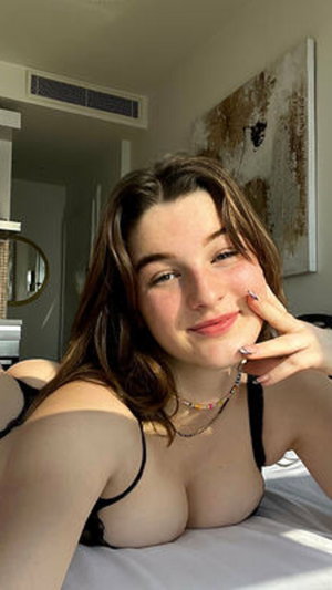 Woman with brown hair in black bra taking bedroom selfie.