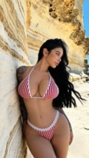 Woman in pink striped bikini leaning against rock at beach.