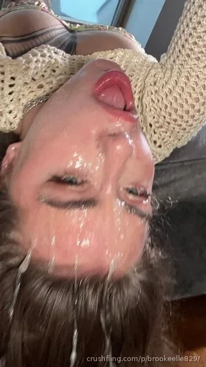 Woman with brown hair lying down, wearing a beige knitted top, face covered in liquid.