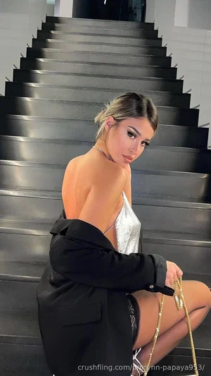 Woman in black blazer and silver top posing on metal stairs indoors.
