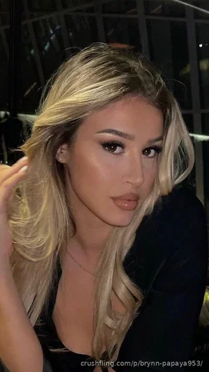 Woman with blonde hair and makeup, wearing black top, indoors.