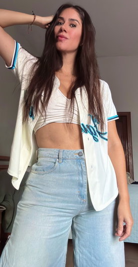 Brunette woman in white crop top and jeans posing indoors.