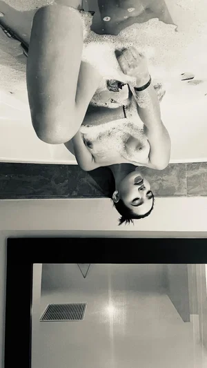 Woman with short hair soaping her body in a bathtub, black and white photo.