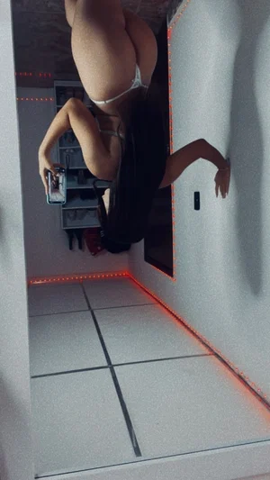 Woman in white lingerie posing in a room with red LED lights, holding phone for mirror selfie.